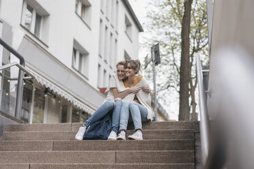 Friends sitting on stairs in the city, sharing cardigan - JOSF02346