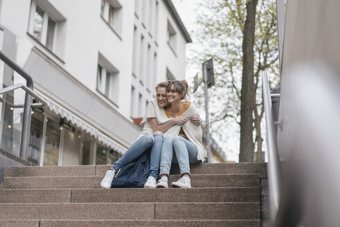 Freunde sitzen auf einer Treppe in der Stadt und teilen sich eine Strickjacke - JOSF02346