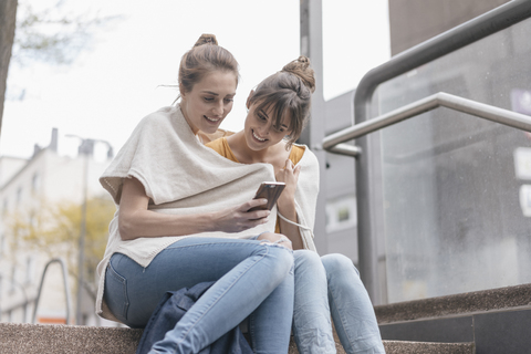 Freunde sitzen auf einer Treppe in der Stadt und benutzen ein Smartphone, lizenzfreies Stockfoto