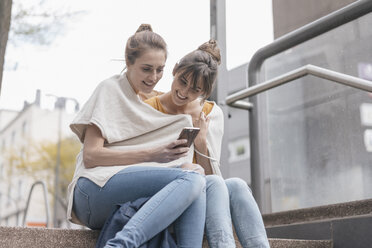 Freunde sitzen auf einer Treppe in der Stadt und benutzen ein Smartphone - JOSF02347