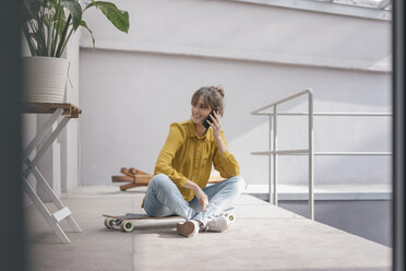 Junge Frau sitzt auf einem Skateboard und benutzt ein Smartphone - JOSF02356