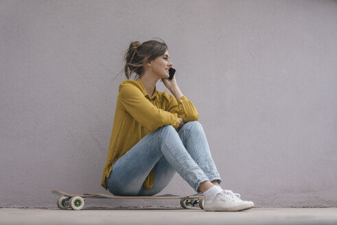 Junge Frau sitzt auf einem Skateboard und benutzt ein Smartphone - JOSF02358