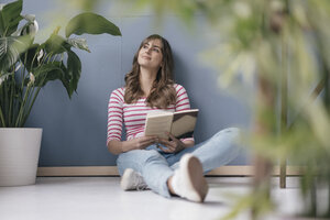 Frau sitzt in ihrem neuen Haus auf dem Boden, liest ein Buch, umgeben von Pflanzen - JOSF02366