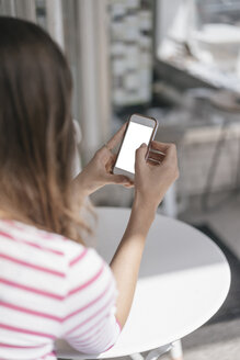 Junge Frau sitzt in einem Café und benutzt ihr Smartphone - JOSF02380