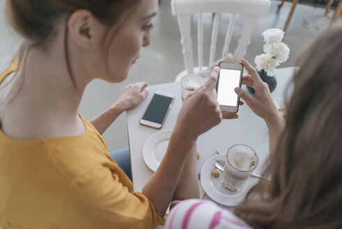 Zwei Freundinnen treffen sich in einem Café und benutzen ihr Smartphone - JOSF02386