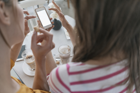 Two girlfriends meeting in a coffee shop, using smartphone stock photo