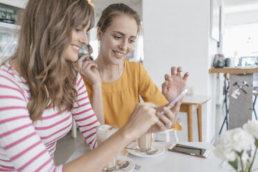 Two girlfriends meeting in a coffee shop, using smartphone - JOSF02389