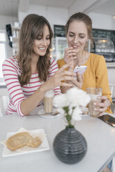 Zwei Freundinnen treffen sich in einem Café und benutzen ihr Smartphone - JOSF02390