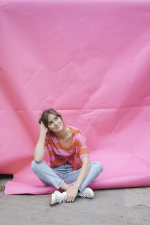 Selbstbewusste junge Frau sitzt auf rosa Hintergrund - JOSF02430