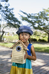 Young girl wearing a summer dress and sun hat, holding a bird house. - MINF02226