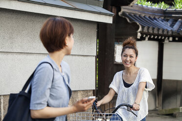 A woman chatting to another woman sitting on a bicycle. - MINF02265