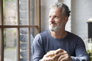 Mture man taking a break, drinking coffee at the window of his loft apartment - FKF03044