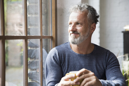 Mture man taking a break, drinking coffee at the window of his loft apartment - FKF03044