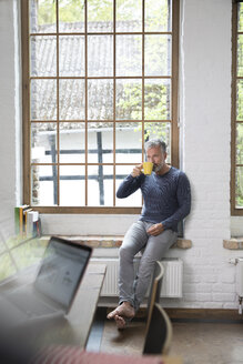 Ein Mann macht eine Pause und trinkt Kaffee am Fenster seiner Loftwohnung - FKF03047