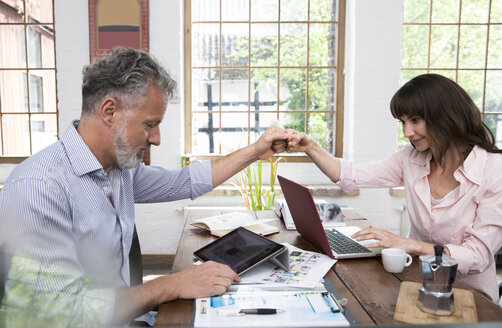 Älteres Paar, das sich im Home-Office mit Laptop und digitalem Tablet die Hand gibt - FKF03071