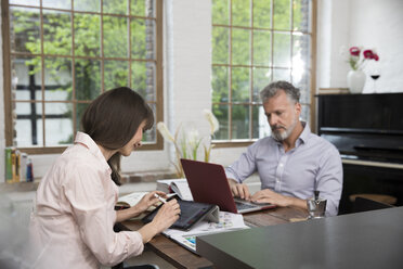 Mature couple working from their home office, using laptop and digital tablet - FKF03072