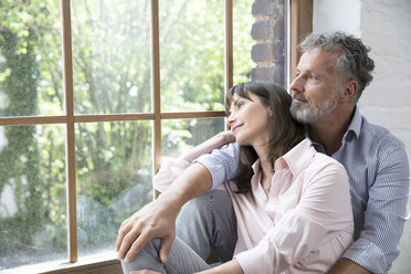 Mature couple sitting on window sill, looking out of window - FKF03081