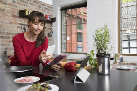 Frau in der Küche scannt Produkte mit ihrem Smartphone, lizenzfreies Stockfoto