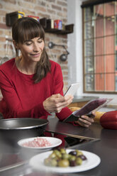 Frau in der Küche scannt Produkte mit ihrem Smartphone - FKF03086