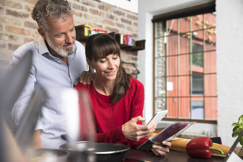 Woman in kitchen scanning products with her smartphone, man looking over her shoulder - FKF03087