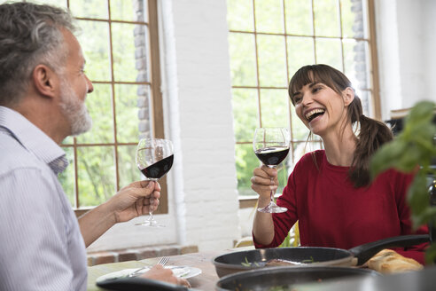 Glückliches Paar sitzt in der Küche, stößt mit Rotwein an und genießt das Abendessen - FKF03098