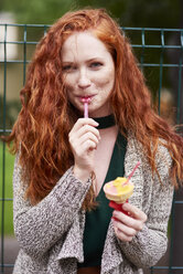 Portrait of smiling redheaded woman eating icecream - ABIF00777