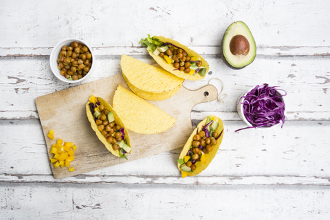 Vegetarische Tacos gefüllt mit in Curcuma gerösteten Kichererbsen, gelber Paprika, Avocado, Salat und Rotkohl, lizenzfreies Stockfoto