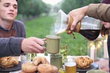 Eine Gruppe von Menschen sitzt an einem Tisch mit Speisen und Getränken und schenkt Kaffee ein. - MINF02299