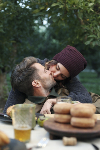 Apfelgarten, ein sich küssendes Paar, Essen und Trinken auf einem Tisch., lizenzfreies Stockfoto
