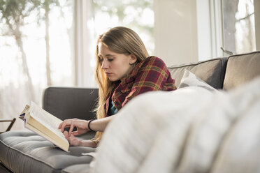 Junge Frau liegt auf einem Sofa und liest ein Buch. - MINF02306