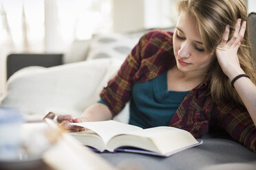 Junge Frau sitzt auf einem Sofa und liest ein Buch. - MINF02307