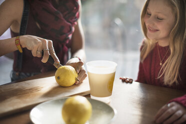 A woman and a smiling girl sitting at a table, woman slicing a lemon in half. - MINF02308