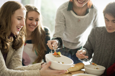 Four people sitting and standing at a table, a woman serving food into a bowl. - MINF02313