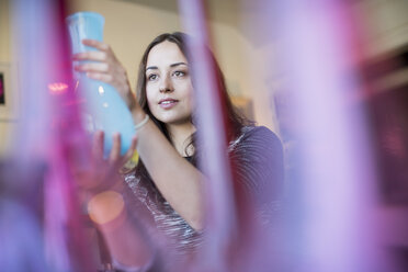 Frau mit einer blauen Glasvase in der Hand, im Vordergrund rote und rosa Vasen. - MINF02314
