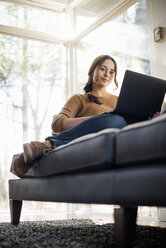 Niedriger Blickwinkel auf eine Frau, die auf einem Sofa sitzt und auf ihren Laptop schaut. - MINF02319