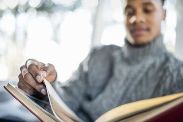 Man wearing a grey roll-neck jumper flipping through the pages of a book. - MINF02325