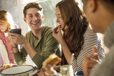 A group of people sitting at a table, smiling, eating, drinking and chatting. - MINF02328