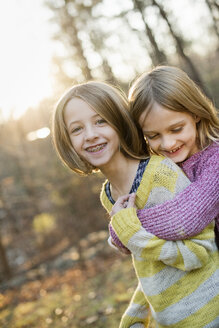 Zwei lächelnde Mädchen in einem Wald, die sich umarmen. - MINF02332