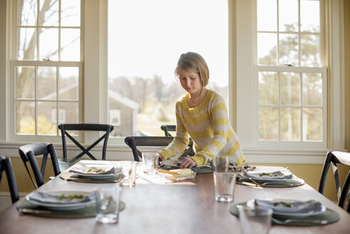 Ein junges Mädchen deckt den Tisch mit Tellern und Besteck. - MINF02339