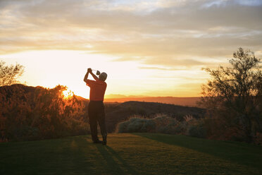 Golfer beim Abschlag in den Sonnenuntergang auf dem Golfplatz. - MINF02357