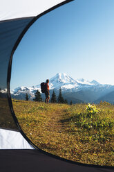 View from inside a camping tent of a man hiking across national forest land with Mount Baker in the distance. - MINF02361