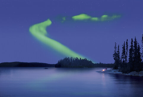 The Northern Lights in the night sky, the Aurora borealis above a calm lake. Two people by a fire on the lake shore. - MINF02366