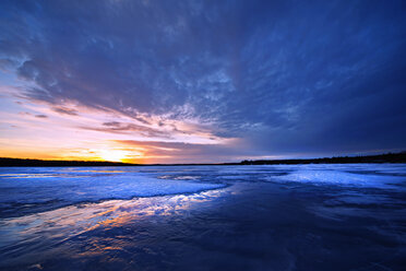 Ein zugefrorener See in der Abenddämmerung und Blick auf die untergehende Sonne am Horizont. - MINF02371