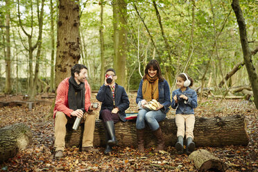 Buchenwald im Herbst: Eltern und zwei Kinder sitzen auf einem Baumstamm und machen ein Picknick. - MINF02460