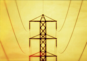 Ein Wasserturm, ein Strommast, eine Metallstruktur mit Armen, die Stromleitungen tragen, vor einem leuchtend gelben Himmel. - MINF02470