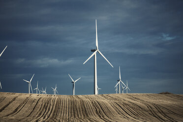 A number of wind turbines reaching into the distance in the farming landscape. Fields of stubble. - MINF02472