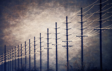 Power lines at regular intervals reaching into the distance against a patch of clearing sky and cloud. - MINF02473