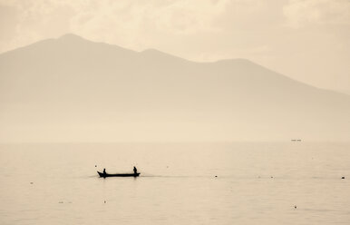 Two people in a small fishing boat on a lake drawing in nets. Mountains in the background. - MINF02474