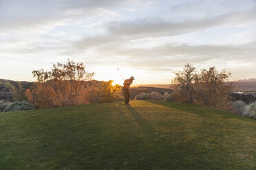 Ein Mann, der von einem Golfabschlag auf einem Golfplatz in den Sonnenuntergang abschlägt. - MINF02504