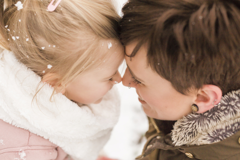 Kleines Mädchen kuschelt mit seiner Mutter im Schnee, lizenzfreies Stockfoto